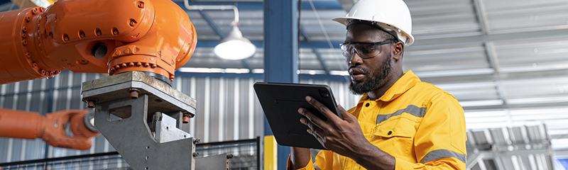 African American engineer working automatic robotic arm machine in factory. Male technician maintenance automatic robotic hand in smart factory, industrial and manufacturing concept.
