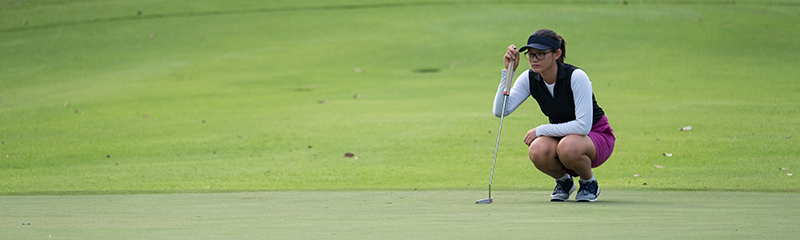 Female golfer lines up her long putt.