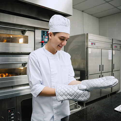 Asian chef putting on protective gloves in commercial kitchen.
