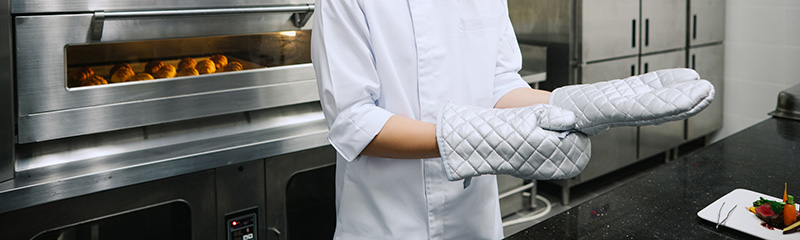 Asian chef putting on protective gloves in commercial kitchen.