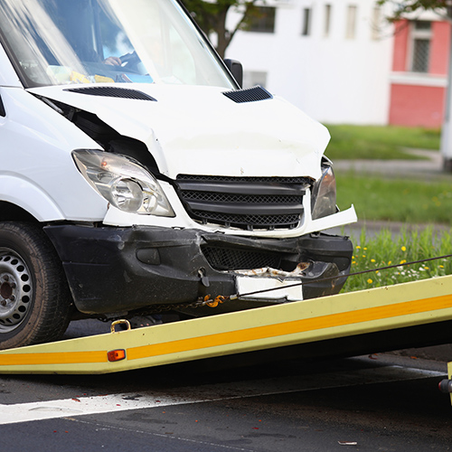 Wrecked white van getting pulled into tow truck. 
