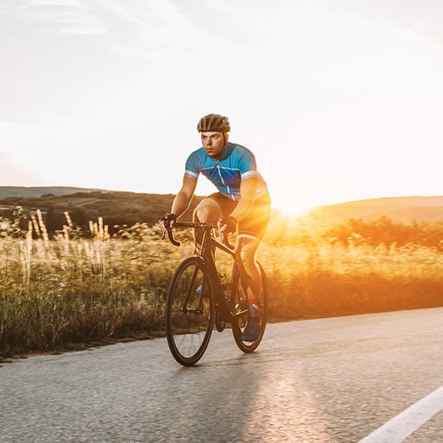 Silhouette of man riding bicycle on road against sky during sunset.