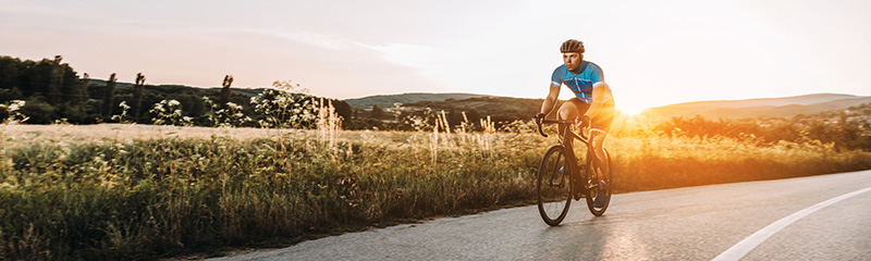 Silhouette of man riding bicycle on road against sky during sunset.