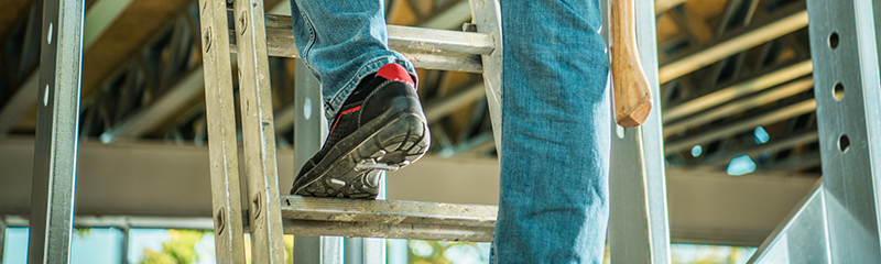 Construction Site Contractor on a Ladder Climbing to Second Floor Keeping Drill Driver in a Hand.