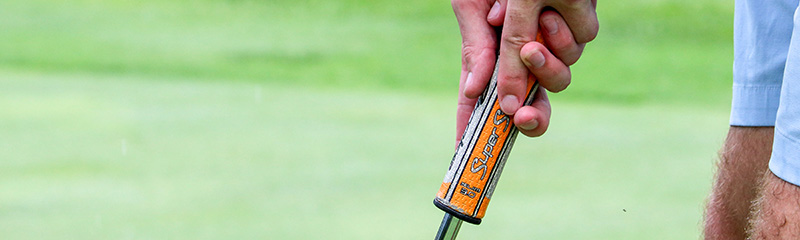 Close up of hands positioned on golf putter grip.