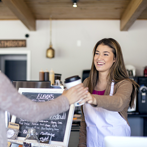 Female barista handing cup of coffee to a patron.