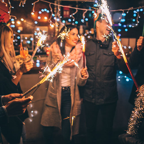 Photo of a cheerful group of friends, at an outdoor New Year's celebration, lightning sparklers at midnight.