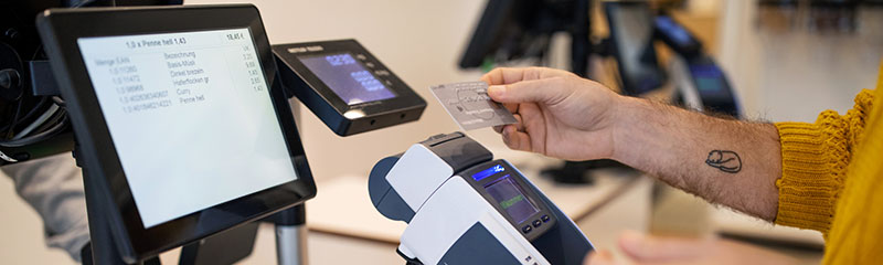 Hand of customer holding credit card for contactless payment at checkout in store.