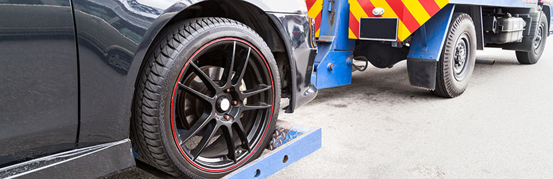 Tow truck towing a broken down car on the street.