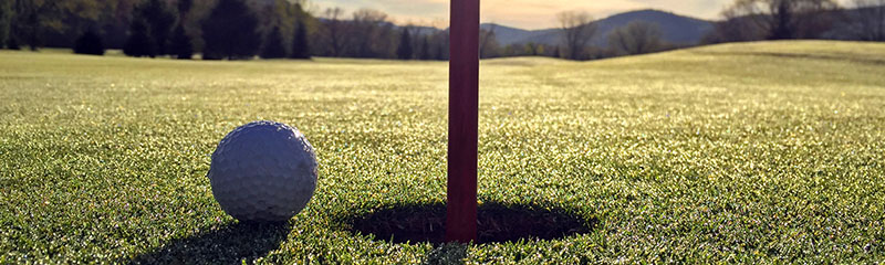 Close up of golf ball near hole with mountain background.