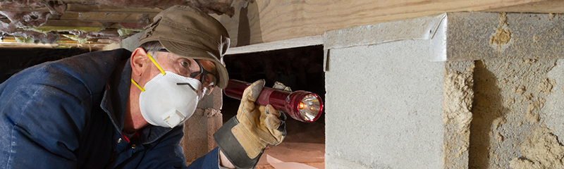 Termite inspector in residential crawl space inspects a pier for termites.