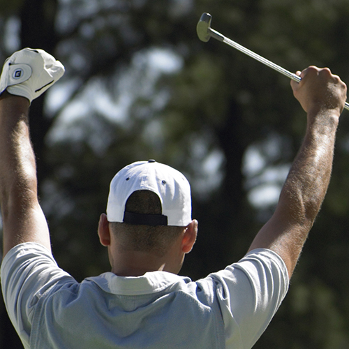 Golfer with gold club in hand and his hands up in celebration.