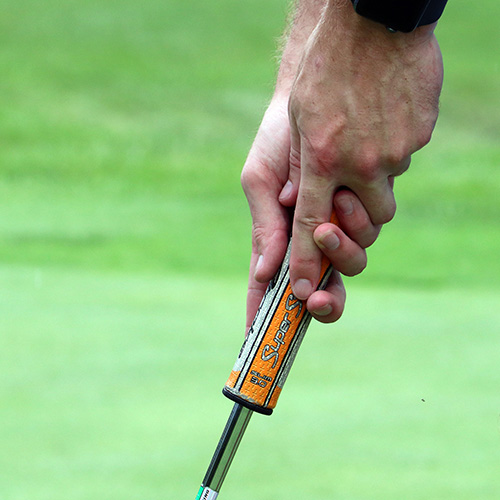 Close up of hands positioned on golf putter grip.