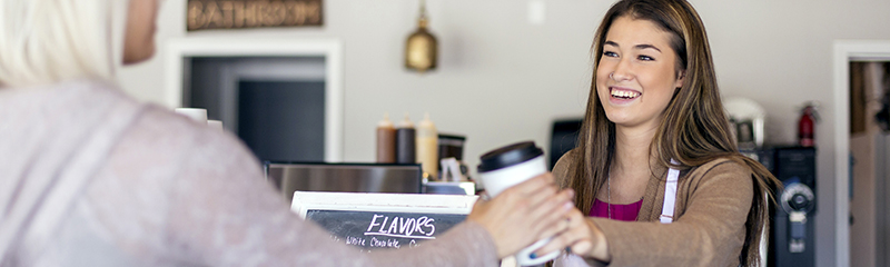 Female barista handing cup of coffee to a patron.