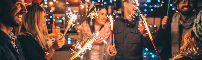 Photo of a cheerful group of friends, at an outdoor New Year's celebration, lightning sparklers at midnight.