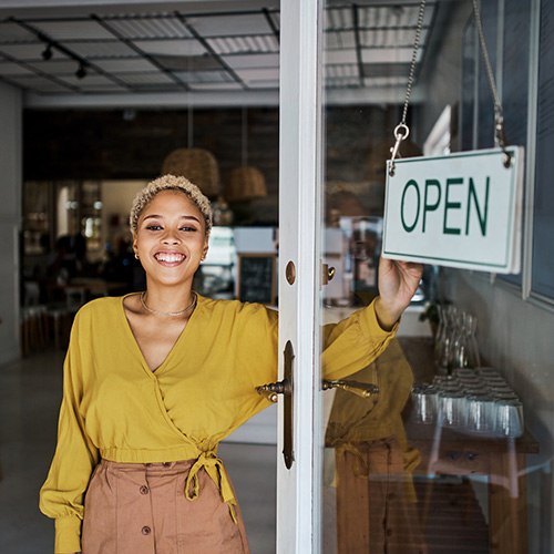 Female small business owner opening her shop or store while looking proud and cheerful. Happy, young and successful African entrepreneur flipping 'open' sign board on the door of her trendy cool cafe.