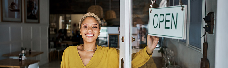 Female small business owner opening her shop or store while looking proud and cheerful. Happy, young and successful African entrepreneur flipping 'open' sign board on the door of her trendy cool cafe. 
