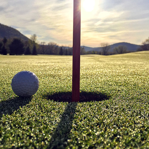 Close-up of golf ball next to hole with mountains in the background.